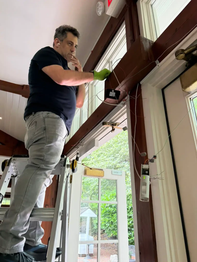 Locksmith technician on a ladder installing door hardware and access control wiring