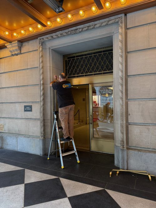 Golden Key Locksmith NYC technician on ladder working on commercial building entrance door during emergency call